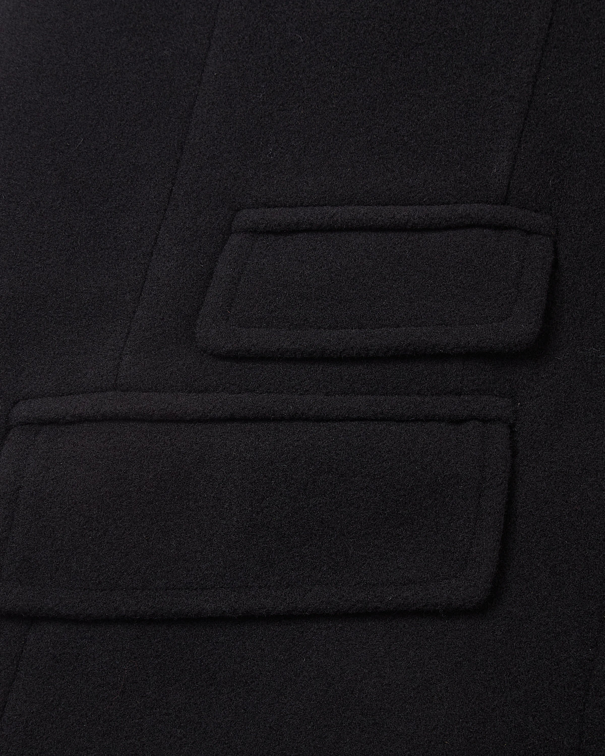 Detail of the double welt flap pockets on the black covert overcoat